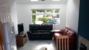 Ein kompakter Wohnraum mit Küchenzeile, einem schwarzen Ledersofa, einem roten Leder-Sofa und einem Esstisch mit Unterlage.