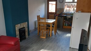 Ein Wohnzimmer mit einem roten Sofa, einem Esstisch mit Stühlen, einem Kamin und einer Küchenzeile mit Kühlschrank und Spüle.