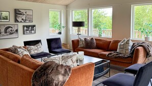 A modern living room with a sofa set, a coffee table, and a TV. There are framed pictures on the wall and a window with a view of greenery. - 4 bedroom nice home in äspered (äspered)