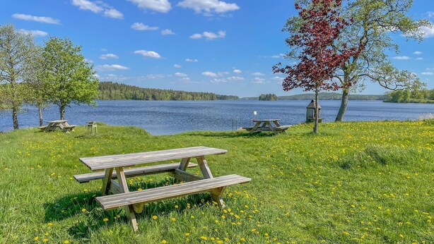A lakeside picnic area with wooden benches and a bird feeder. - 4 bedroom nice home in äspered (äspered)