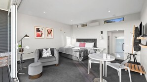 A modern hotel room with a bed, a sofa, a dining table, and a TV. - The Nest- Luxury Pod w King bed + private spa (Point Lonsdale)