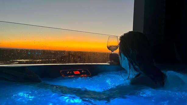 A hot tub with a control panel and a glass of wine, overlooking a sunset. - The Nest- Luxury Pod w King bed + private spa (Point Lonsdale)
