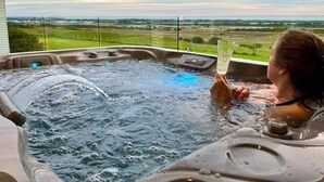 A person relaxing in a hot tub with a view of a green landscape and a cloudy sky. - The Nest- Luxury Pod w King bed + private spa (Point Lonsdale)