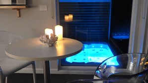 A modern room with a glass table, a clear chair, and a visible jacuzzi area with blue lighting. - The Nest- Luxury Pod w King bed + private spa (Point Lonsdale)