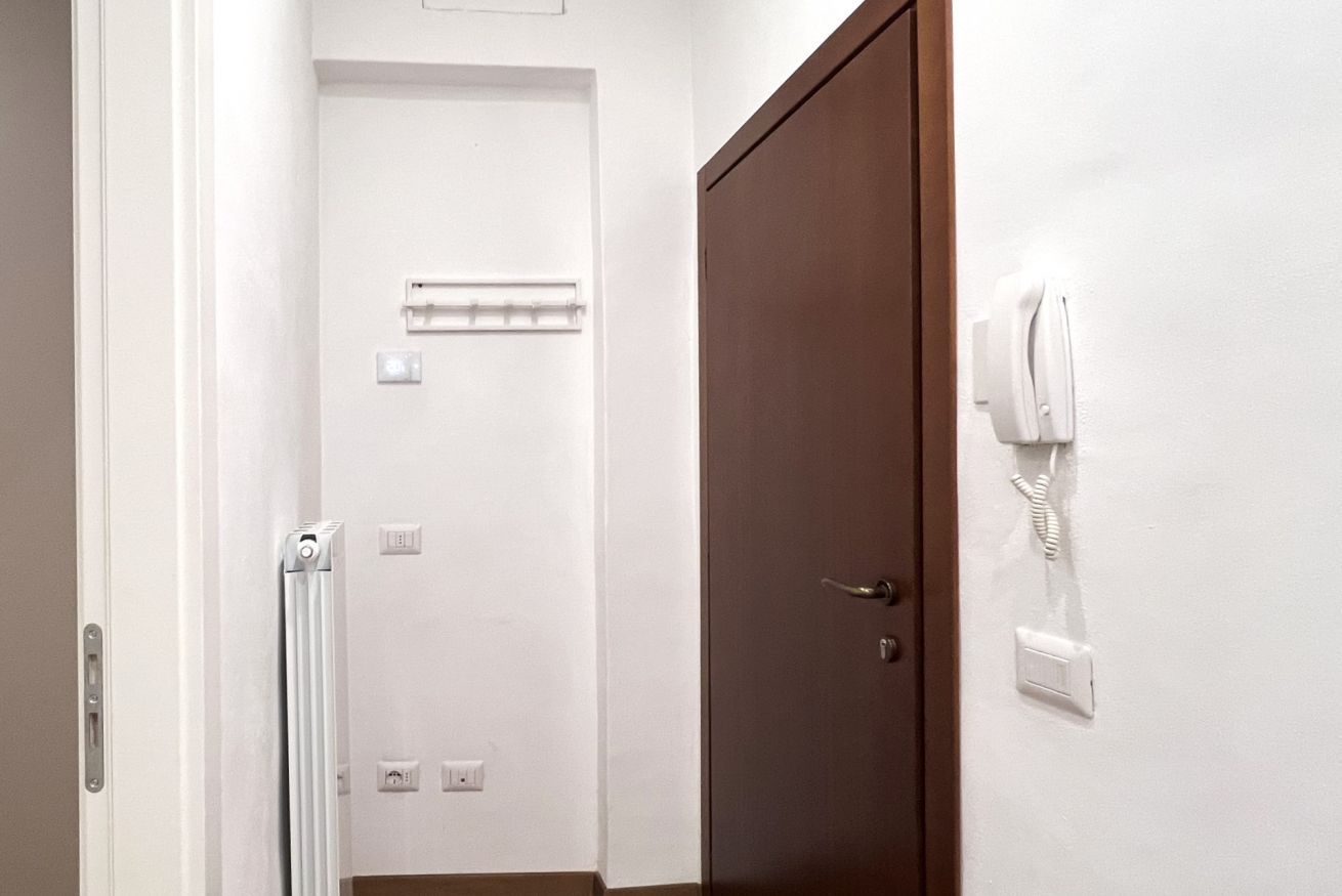 A hotel room with a wooden door, a white radiator, and a telephone mounted on the wall.