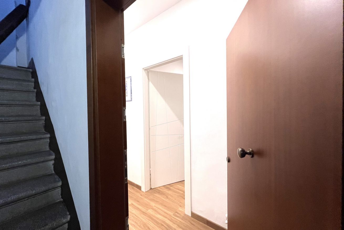 A hallway with a wooden staircase, a closed door, and a tiled floor.