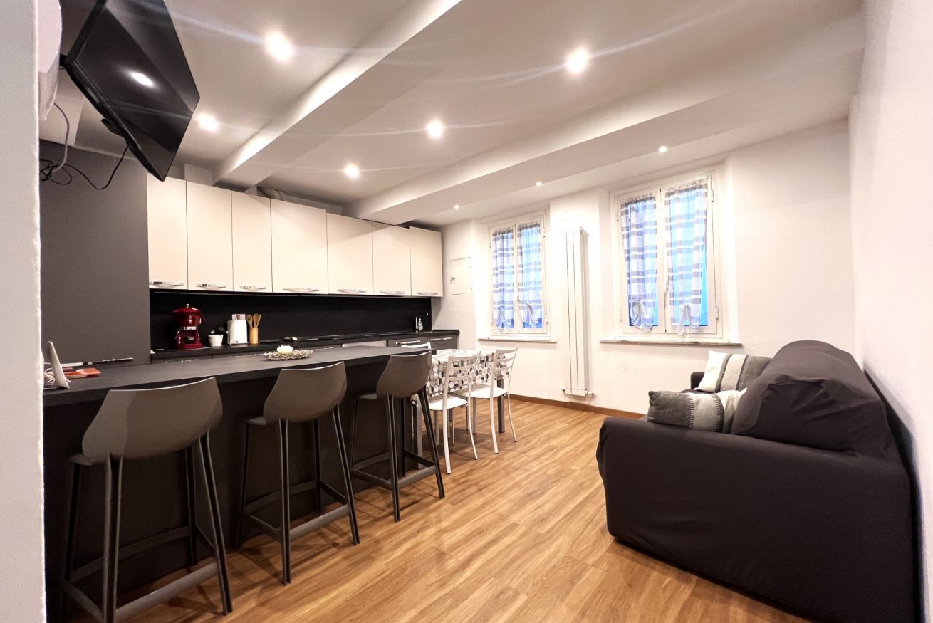 Una cocina moderna con barra, suelo de madera y un sofá en una sala de estar con ventanas.