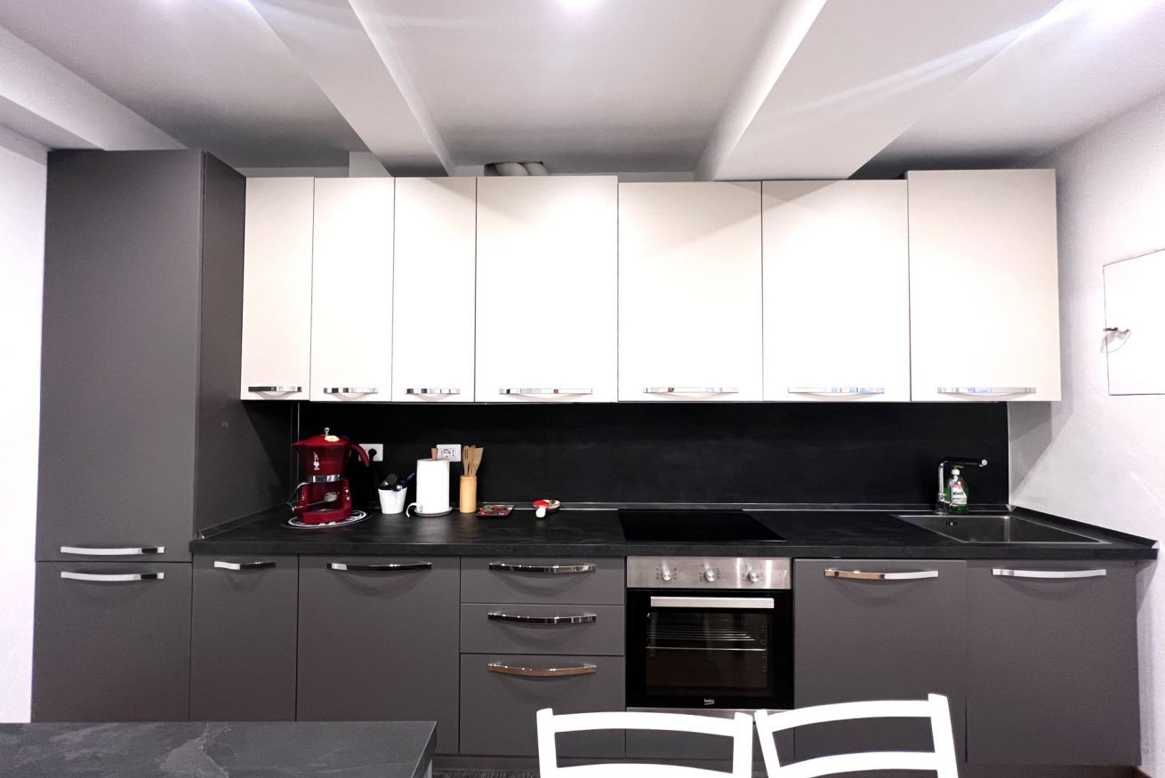 A modern kitchen with grey cabinets, a black countertop, a red coffee maker, and a built-in oven.
