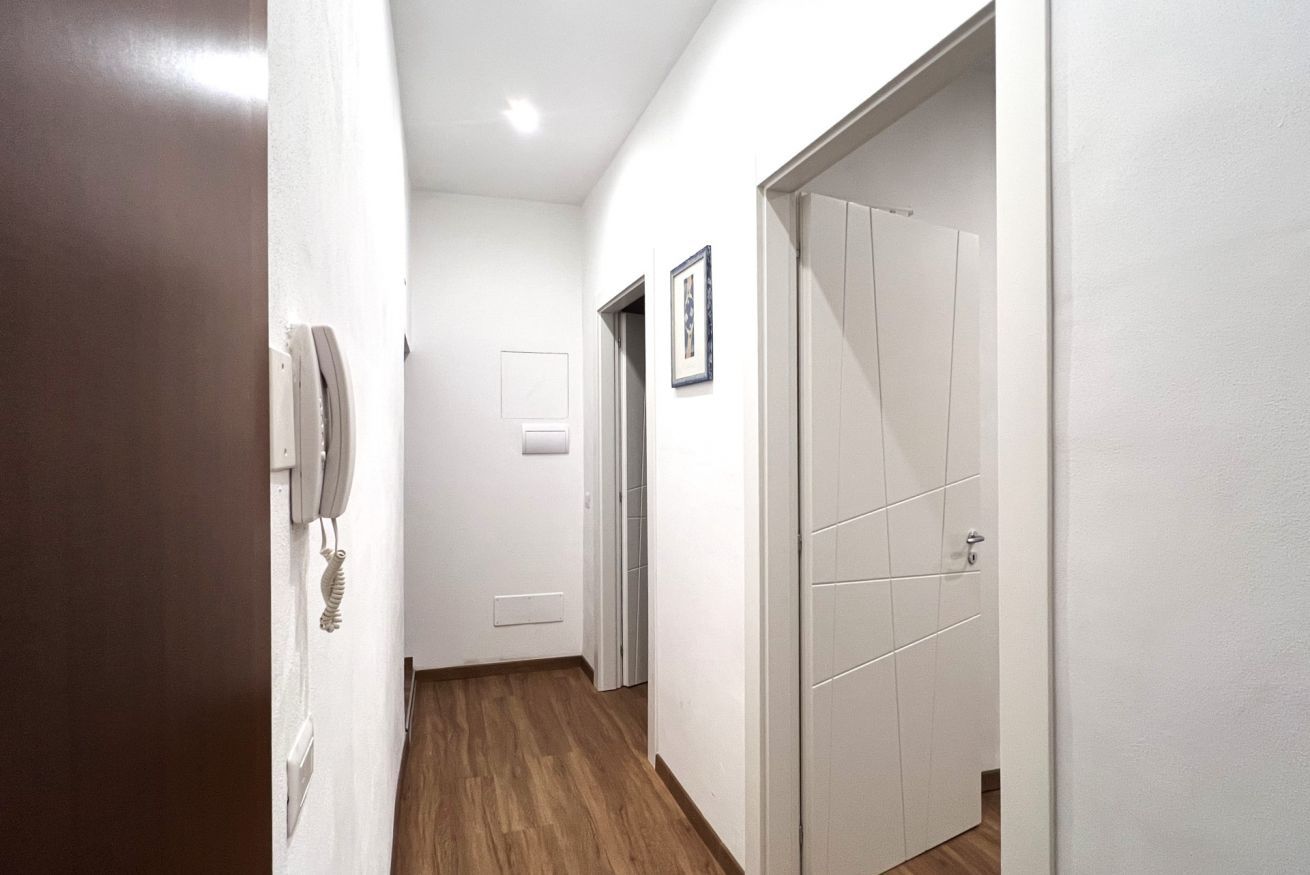 Un corridoio con pareti bianche, pavimento in legno e una porta chiusa con maniglia.
