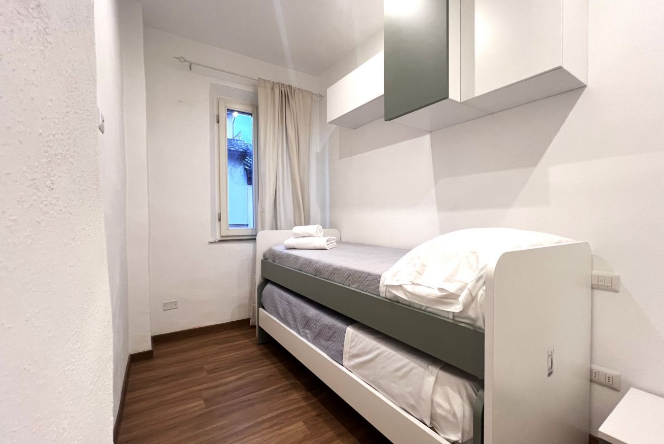 A small, modern bedroom with a bunk bed, a window with curtains, and a built-in wardrobe.