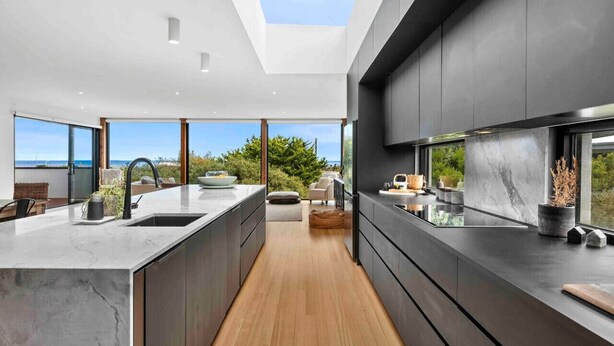 A modern kitchen with a large island, dark cabinetry, and a skylight.