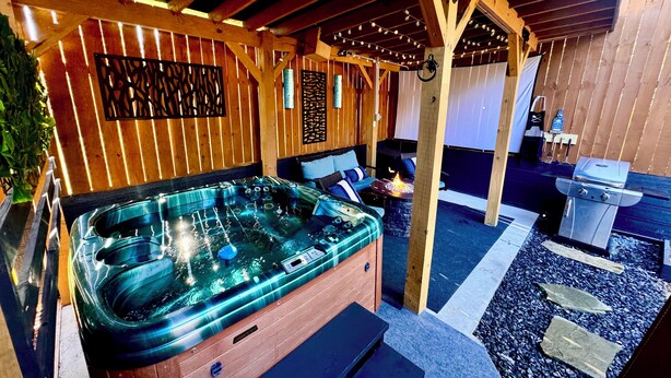 Ett bubbelbad med en trädäckad terrass, en eldstad av sten och ett område med grill.