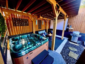 Ein Whirlpool mit einer Holzterrasse, einer Feuerstelle aus Stein und einem Grillbereich.