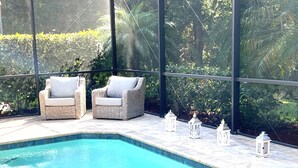 Zona de piscina con dos sillas de mimbre y tres faroles blancos.