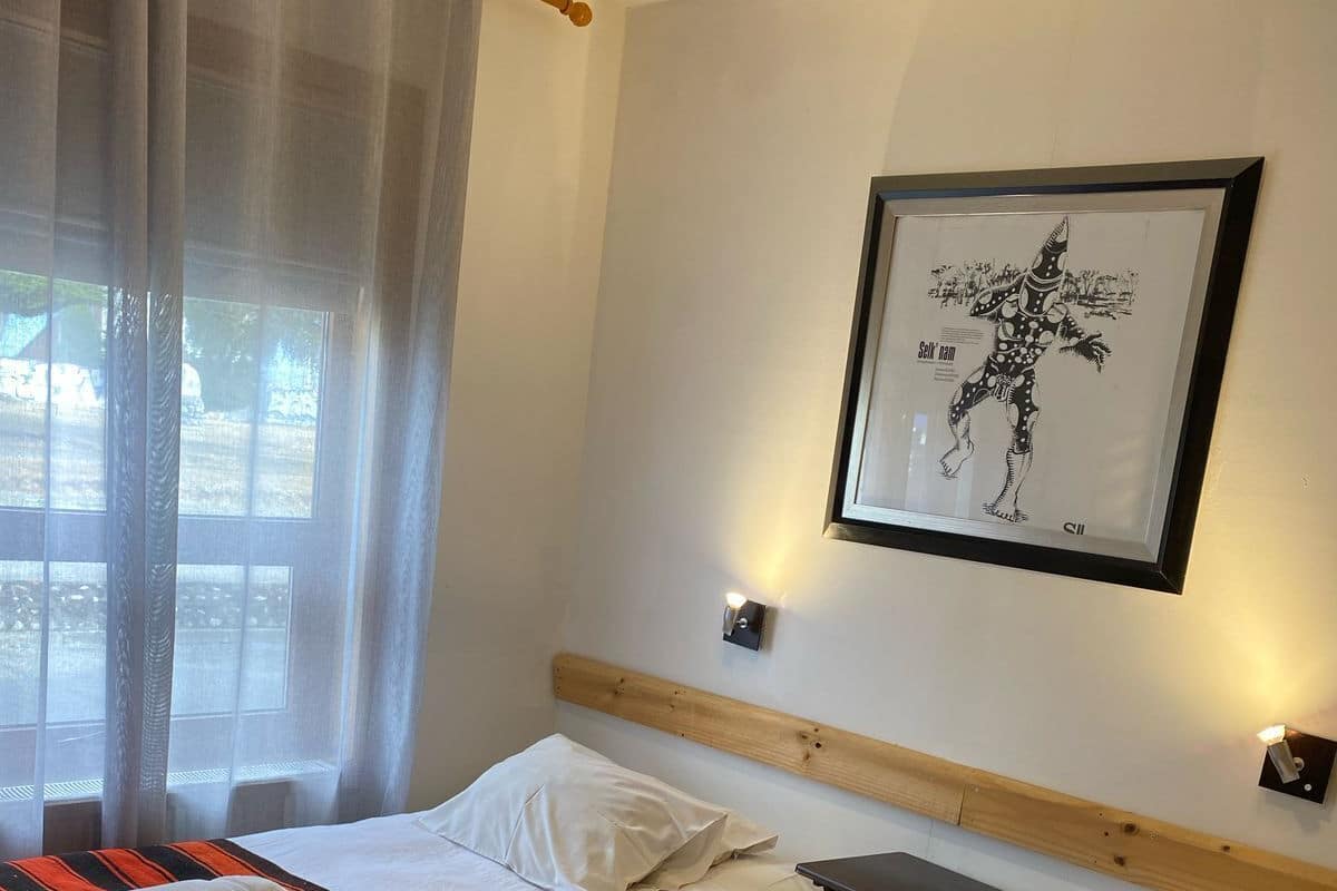 A hotel room with two beds, a small table, and a framed artwork on the wall.