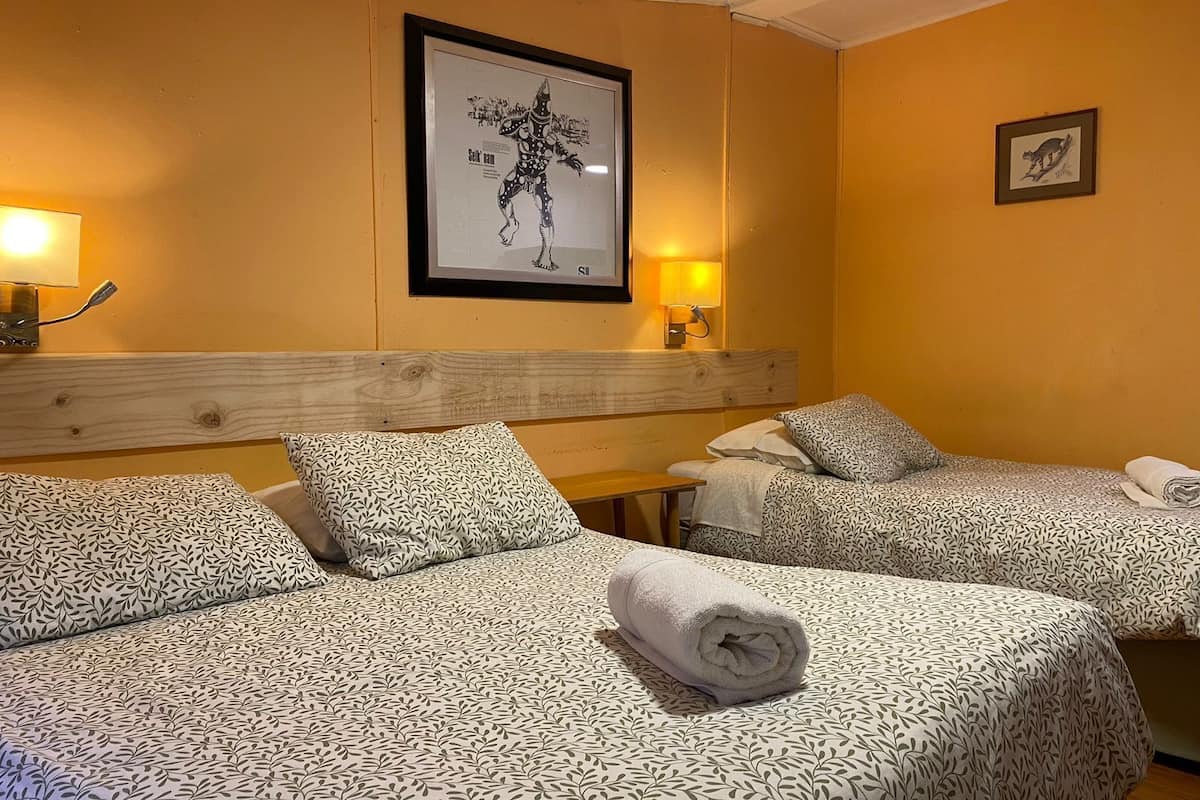 A hotel room with two beds, a wooden headboard, a framed artwork on the wall, and two wall-mounted lamps.