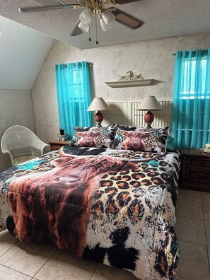 Relax in this serene bedroom with a large bed, ceiling fan, and comfortable wicker chair.