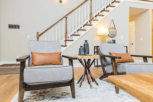 A living room with two grey armchairs, a wooden coffee table, and a staircase with white railings.