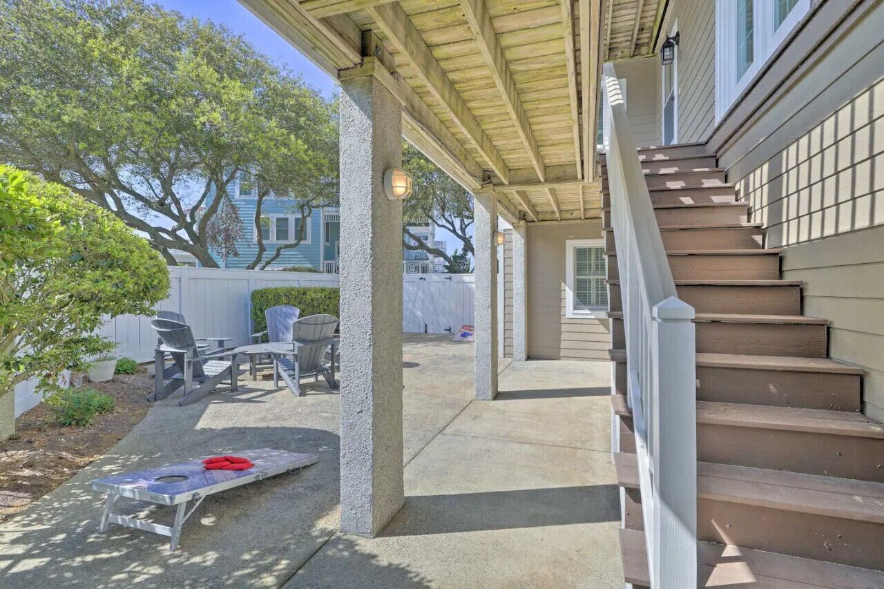 A covered outdoor patio with a concrete floor, a wooden staircase, and a seating area with chairs and a table.