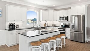 Une cuisine moderne avec des meubles blancs, des appareils en acier inoxydable et un grand îlot central doté de tabourets.