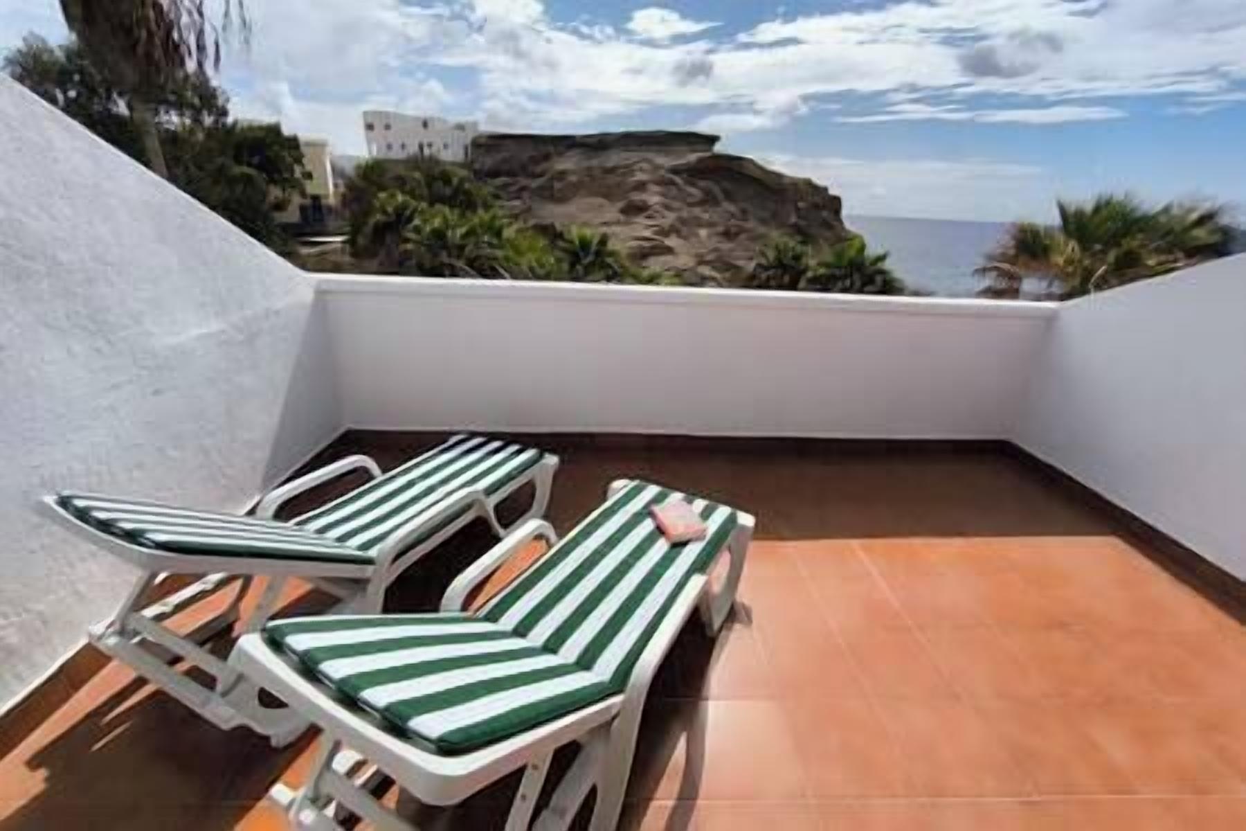 Une terrasse sur le toit, avec deux chaises longues à rayures et une vue sur l’océan et le paysage rocheux.