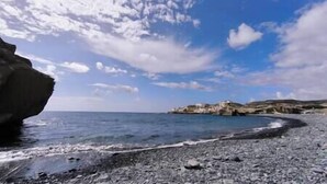 Una spiaggia rocciosa con cielo sereno e un promontorio roccioso in lontananza.