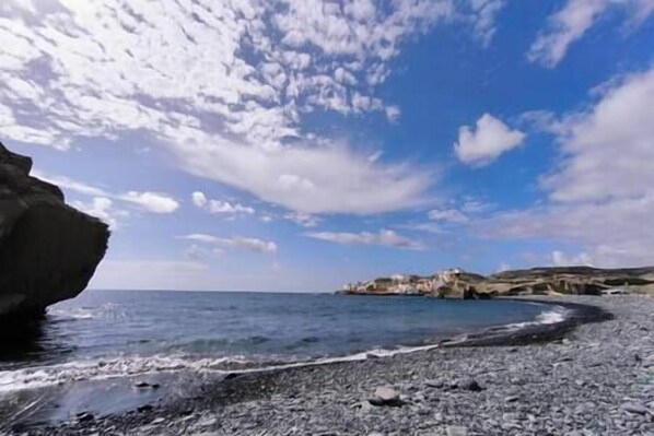Una playa rocosa con cielo despejado y un afloramiento rocoso distante.