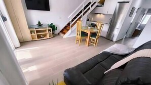 Un soggiorno moderno con un divano nero, un tavolo da pranzo in legno, sedie e una scala che conduce a un livello superiore.
