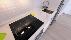 Una cucina moderna con piano cottura a induzione nero, lavello in acciaio inossidabile e piano di lavoro bianco.