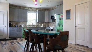 A kitchen with grey cabinets, a green refrigerator, and a dining table with chairs. - The Board House "Longboard" (Galveston)