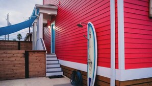 A red building with a wooden deck and a surfboard leaning against it. - The Board House "Longboard" (Galveston)
