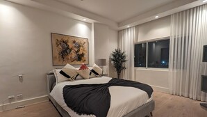 Ein modernes Schlafzimmer mit einem großen Bett, einem Deckenventilator, einem Fenster mit Vorhängen und einem Gemälde an der Wand.