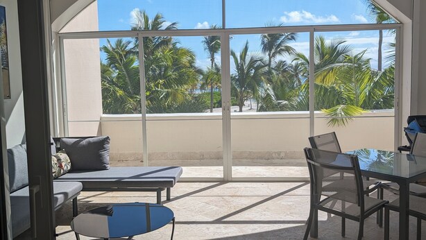 Ein geräumiger Balkon mit Deckenventilator, einem Glastisch mit Stühlen und einer Couch mit Kissen.