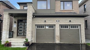 Une maison à deux étages avec une façade en pierre, deux portes de garage et une entrée principale avec des marches.