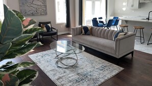 Un salon moderne avec une table basse en verre, un canapé beige et un coin repas avec des chaises bleues.