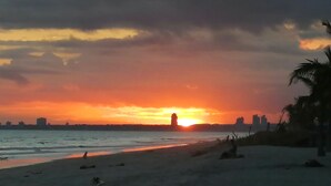 Une plage au coucher du soleil, avec la silhouette d’une ville en arrière-plan.