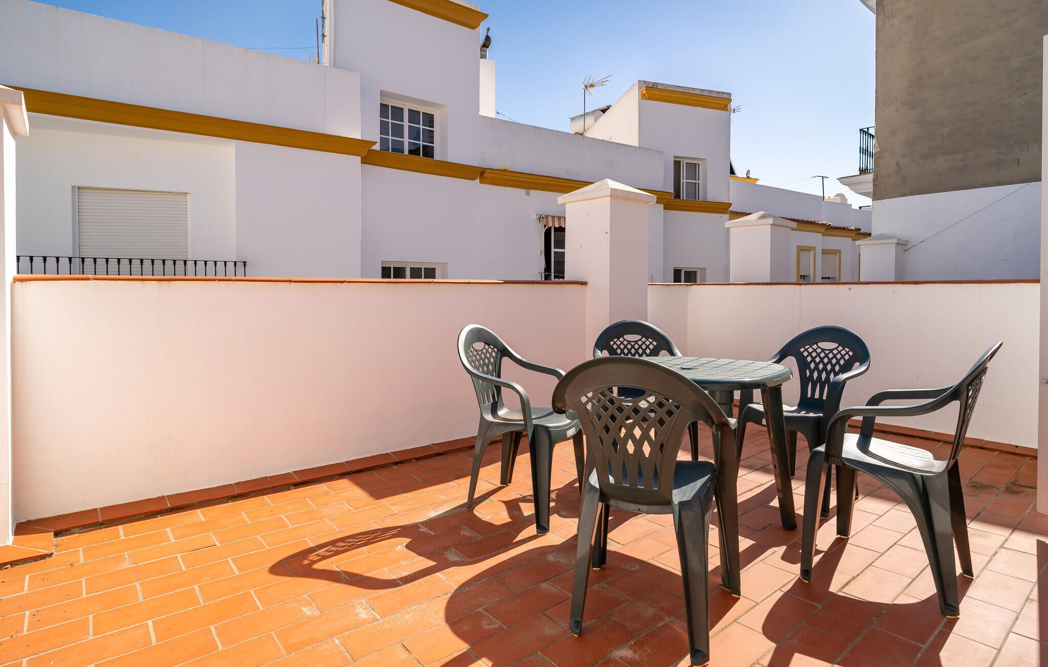 An outdoor patio with a table and chairs, surrounded by white walls and a tiled floor.
