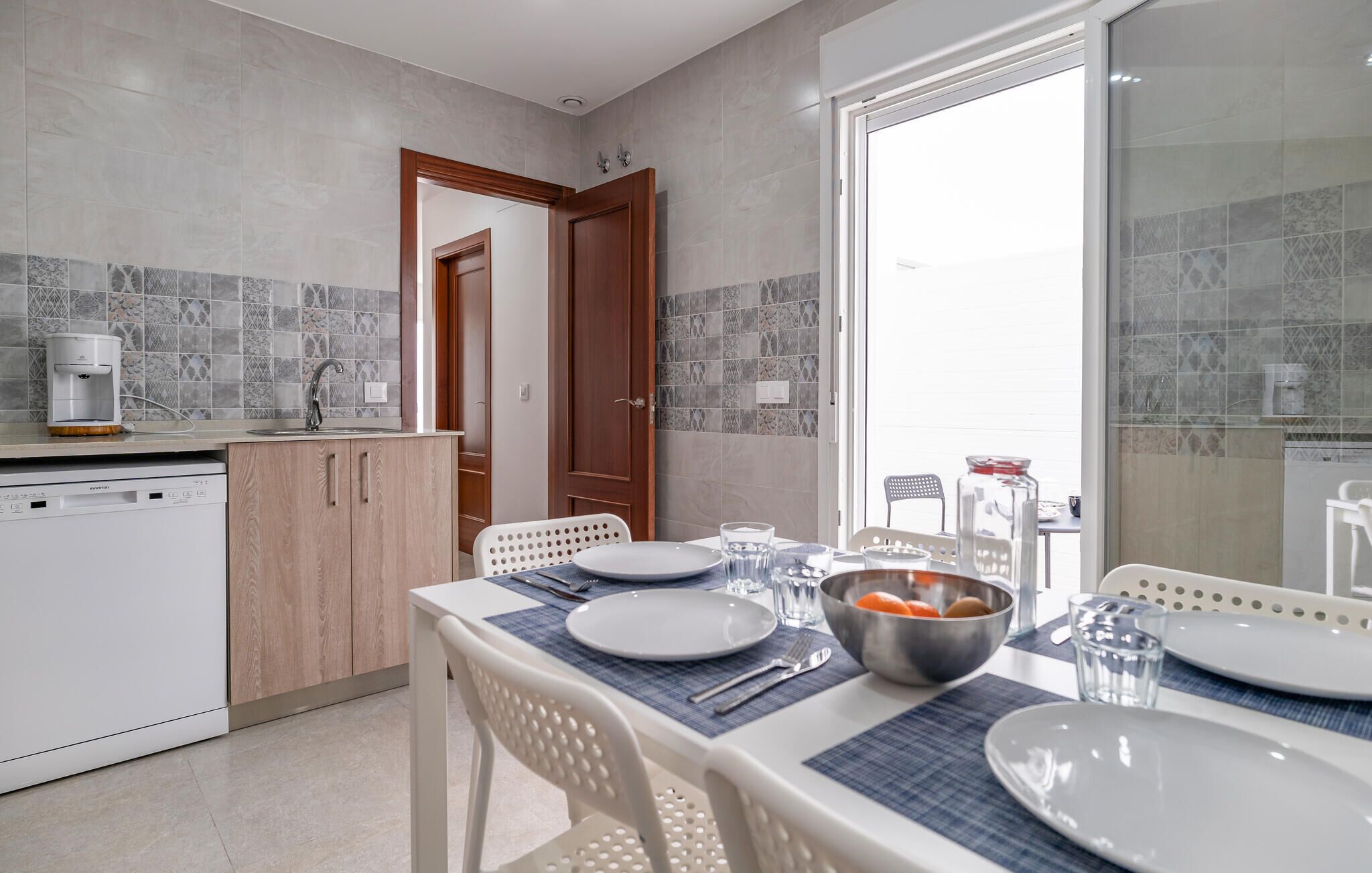 A modern kitchen with a dining area, featuring a coffee machine, a sink, and a dining table set for four.