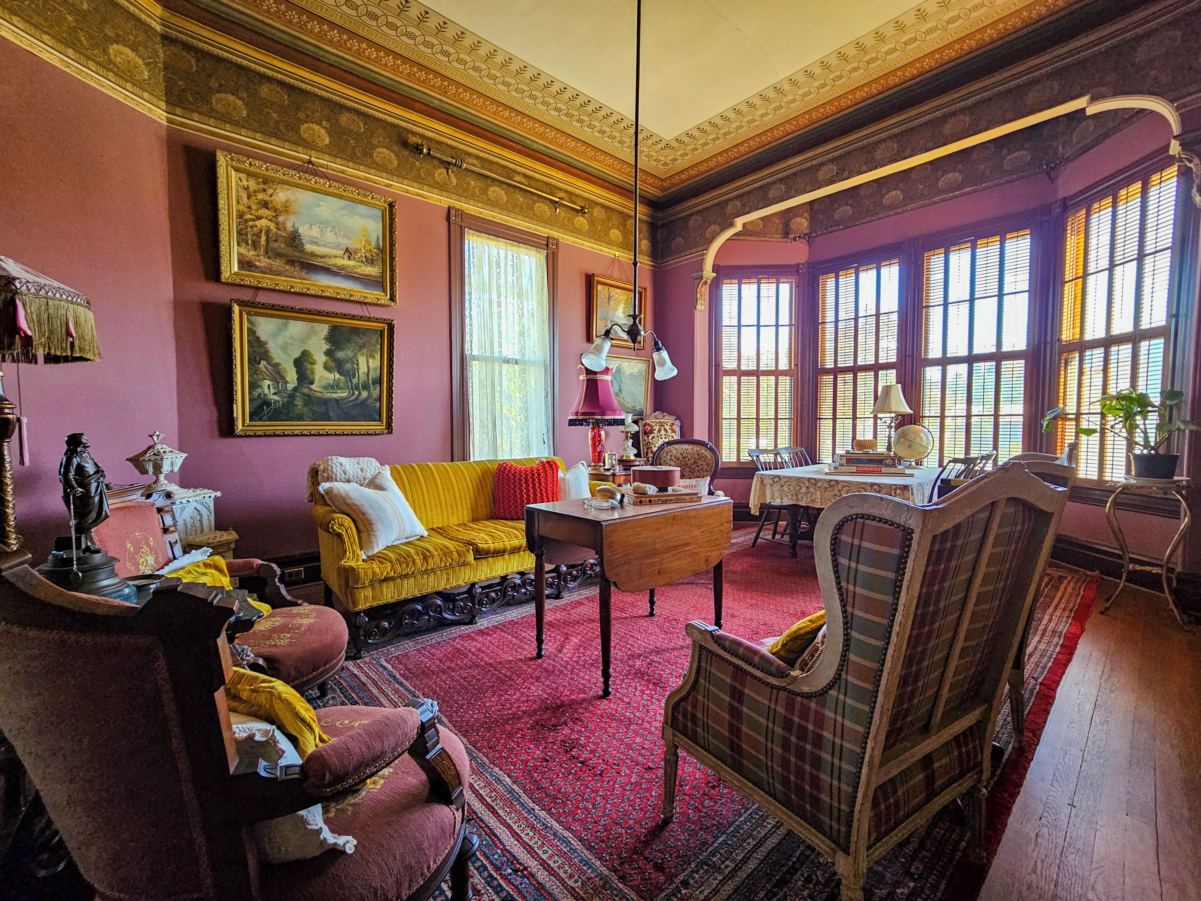 A room with a yellow sofa, a plaid armchair, a wooden table, and a red carpet.