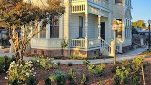 A two-story Victorian-style house with a wrap-around porch, a front entrance with a staircase, and a small front yard with flowers and shrubs. - The JD Hyde Historic Inn (Visalia)