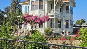 A two-story Victorian-style house with a balcony, surrounded by lush gardens and a clear blue sky. - The JD Hyde Historic Inn (Visalia)