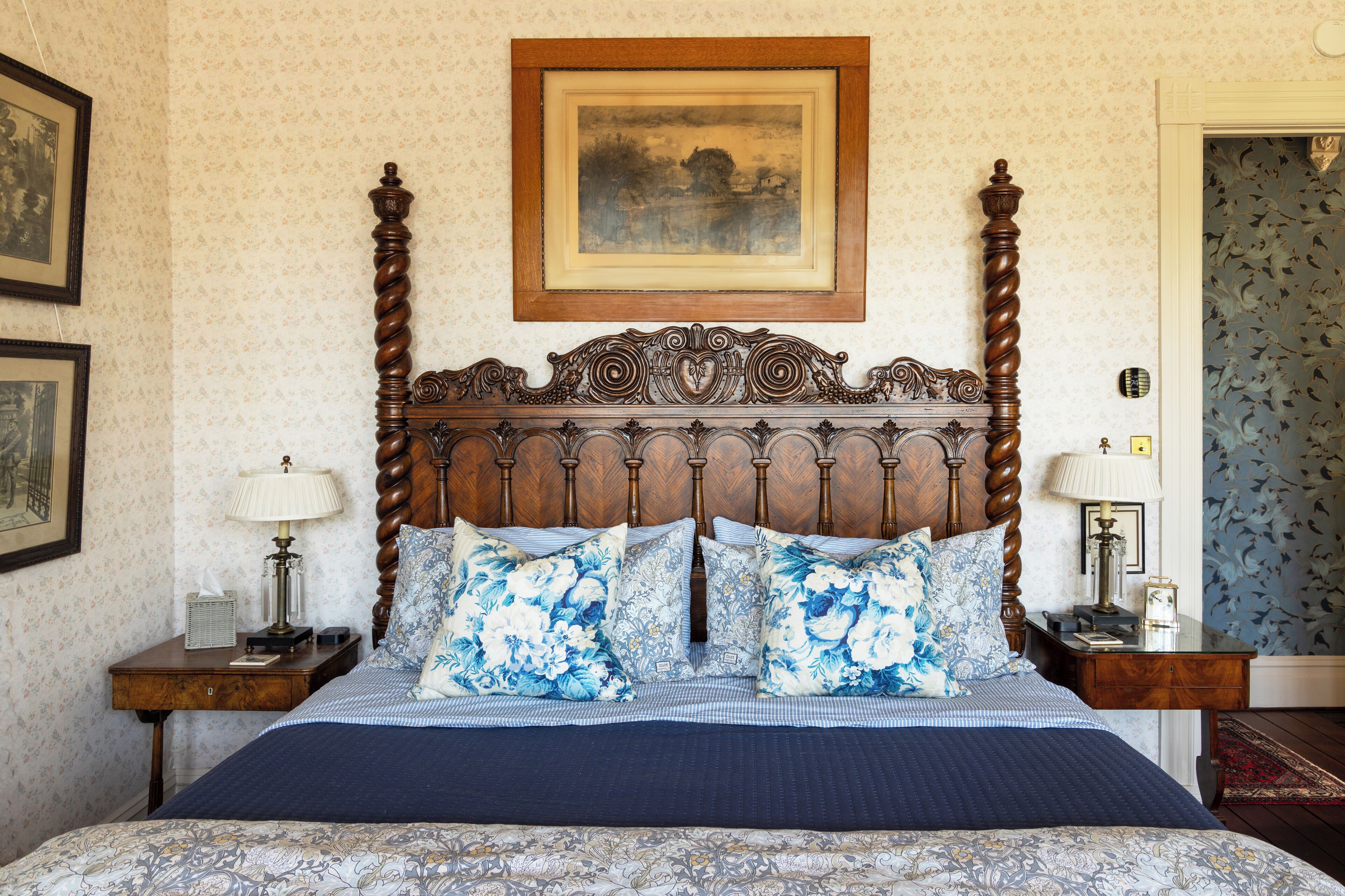 Una cama bien hecha con ropa de cama floral, un cabecero de madera y dos mesitas de noche con lámparas.