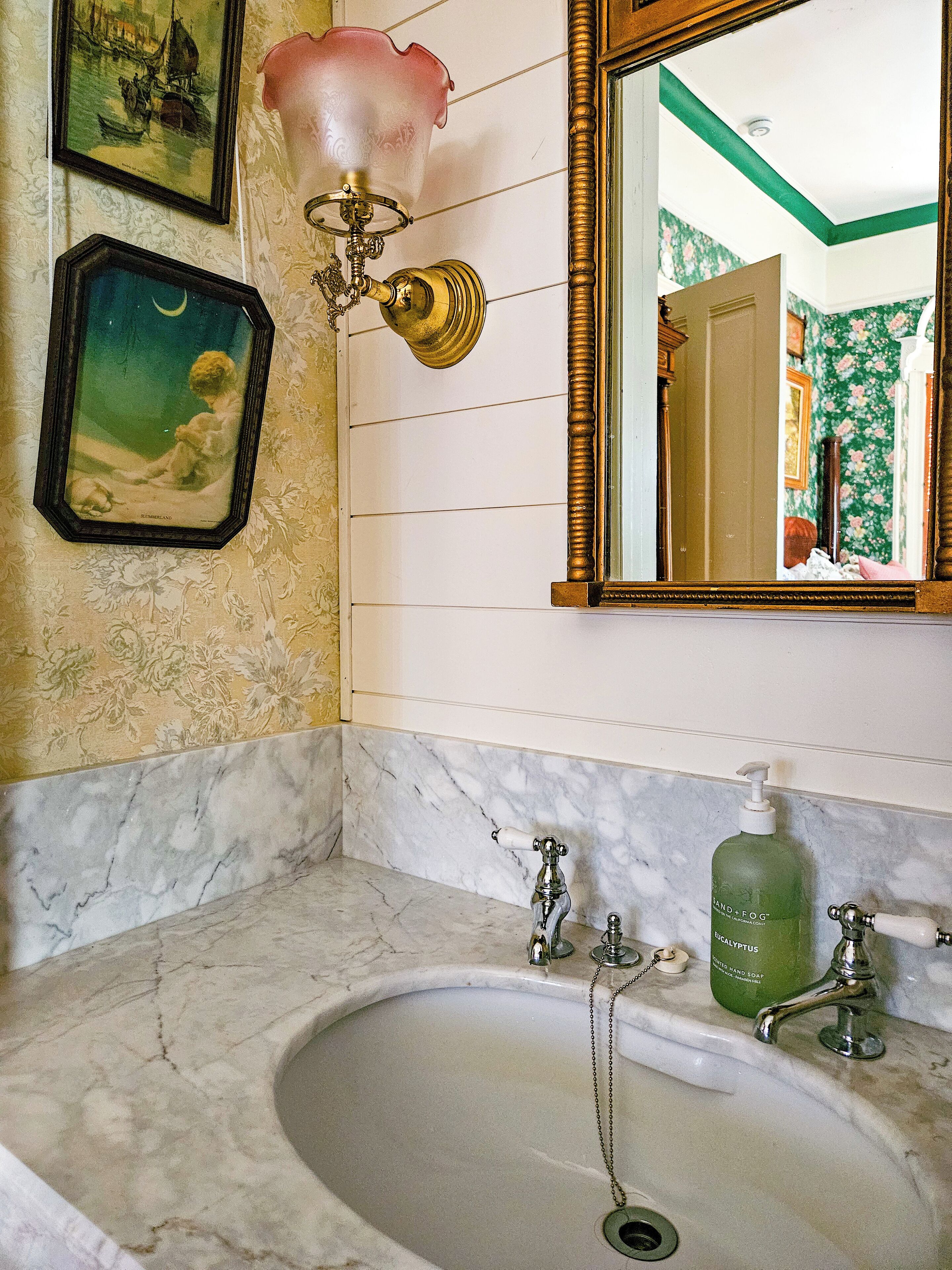 A bathroom with a marble sink, a mirror, and a wall-mounted light fixture.
