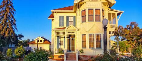 A large, two-story house with a prominent front porch, a driveway, and a well-maintained garden with various plants and a lawn.