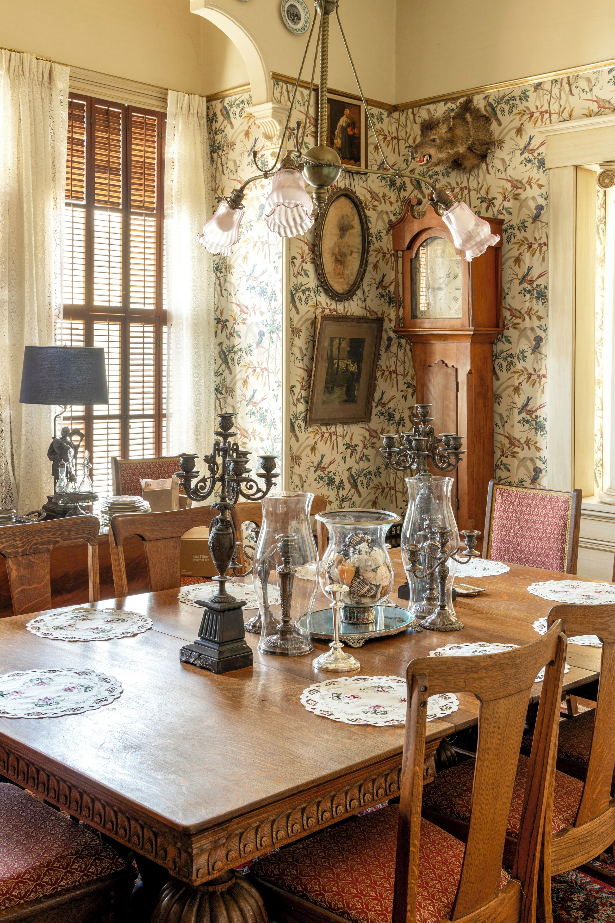 A dining room with a wooden table, chairs, and floral wallpaper.