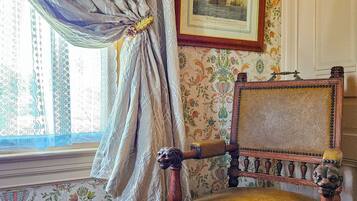 A vintage chair with a floral cushion, a framed picture of a ship, and patterned wallpaper.