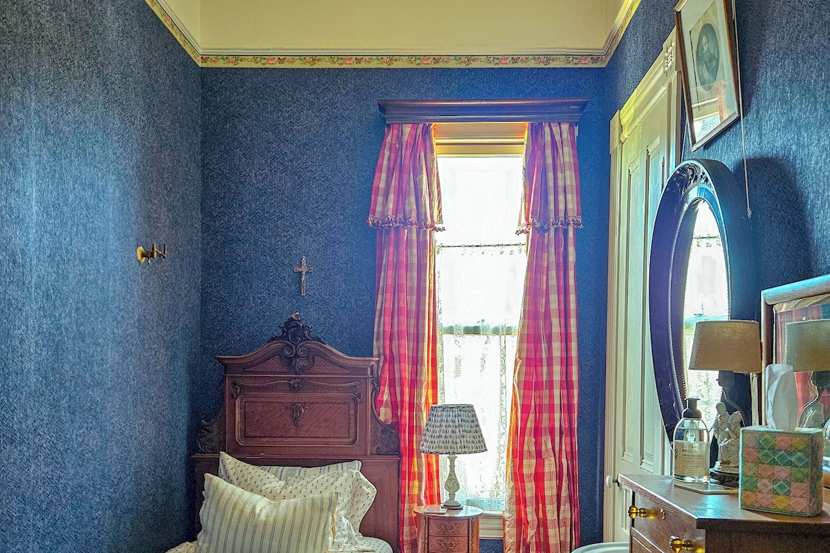A bedroom with a bed, a dresser, a nightstand, a window with curtains, and a mirror.