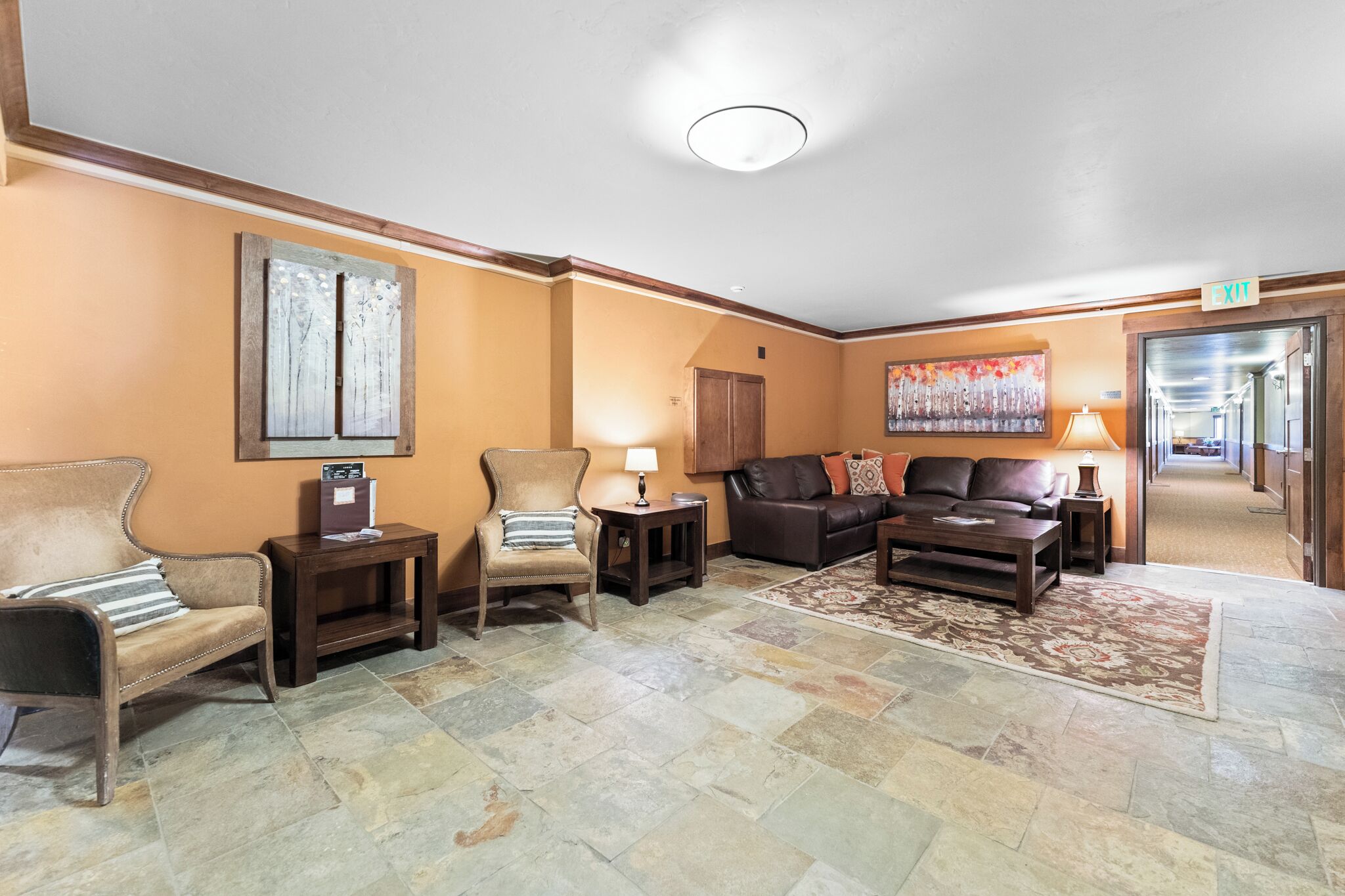 A lobby with a brown leather sofa, a beige armchair, a wooden side table, and a patterned rug.