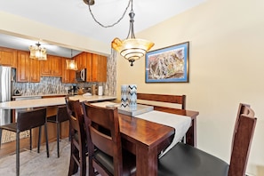 A modern kitchen with wooden cabinets, a central island, and a dining area with a table and chairs. - Cv112c-2 (Copper Mountain)