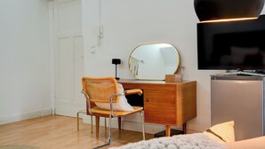 Una camera da letto con una cassettiera in legno, una sedia, uno specchio, una televisione e un frigorifero.